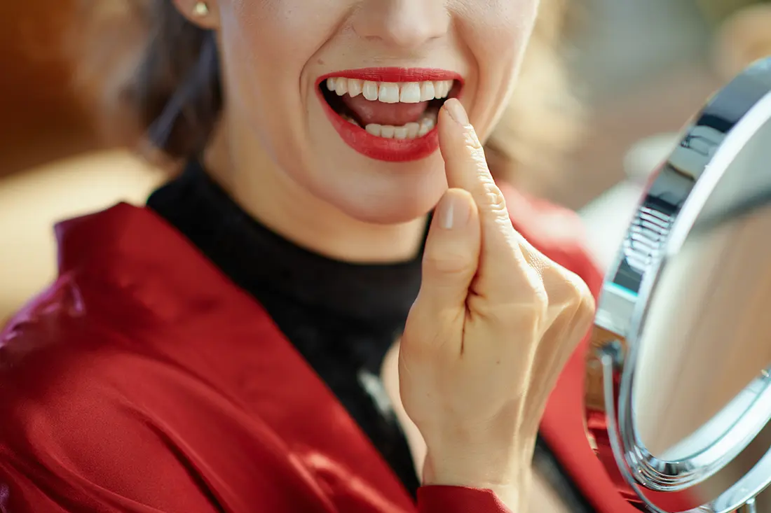 Woman checking her front teeth in a hand mirror