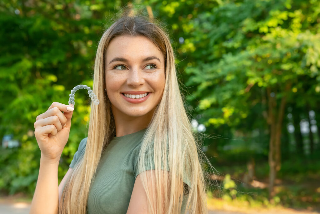 Closeup of beautiful happy smiling woman holding invisible braces.
